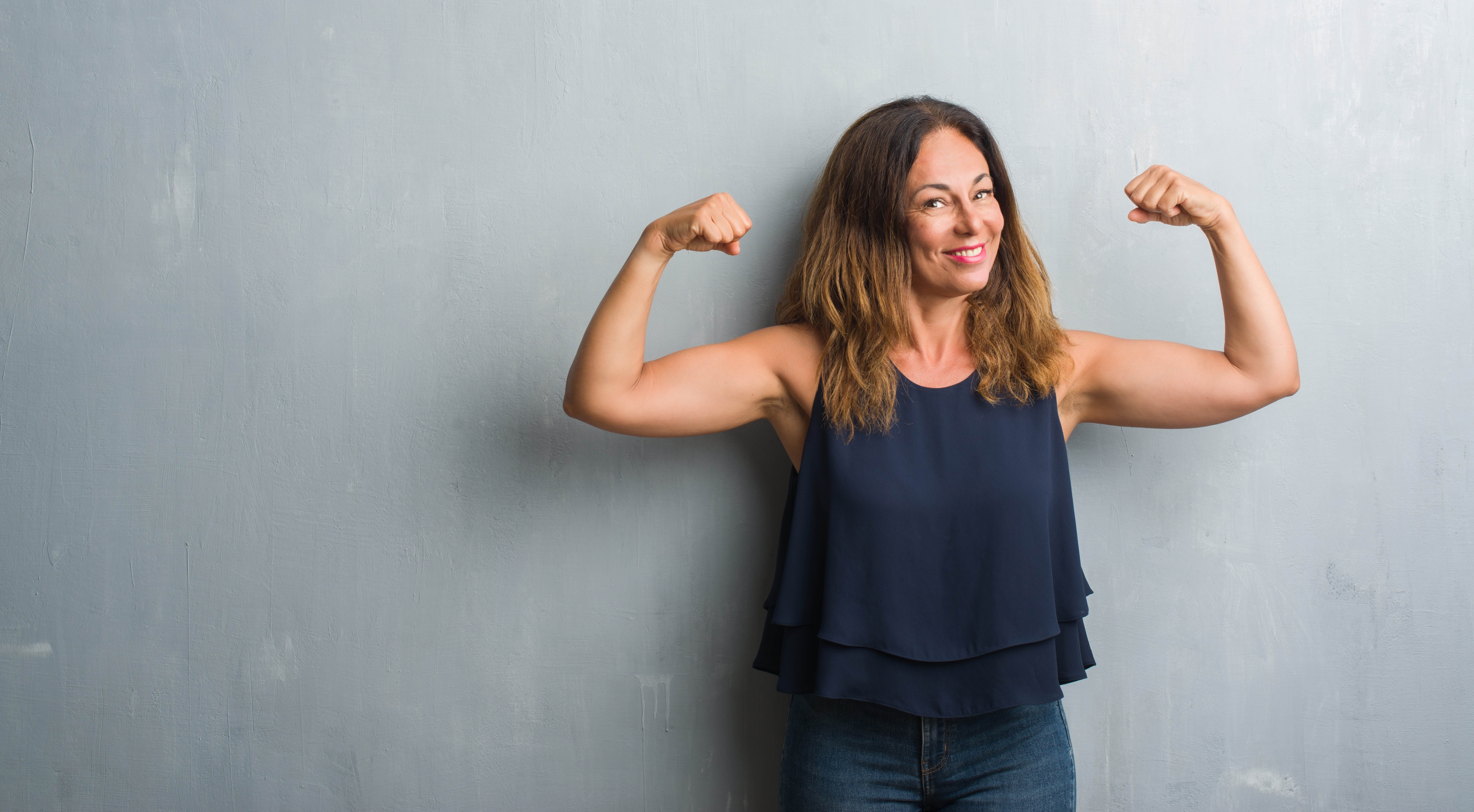 Strong, fit middle aged woman flexing in front of a grey background Strong, fit middle aged woman flexing in front of a grey background